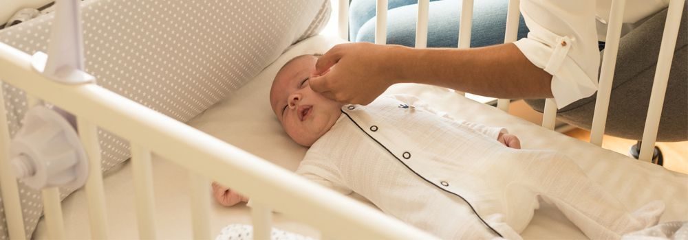 bébé dort dans son berceau, la main de sa maman caresse sa joue